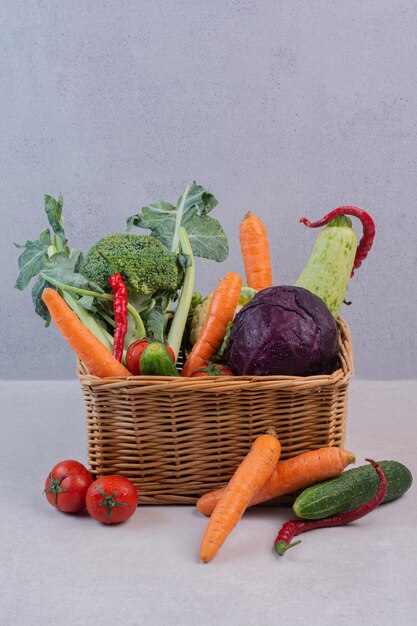 Panier en bois de légumes frais sur une surface blanche.