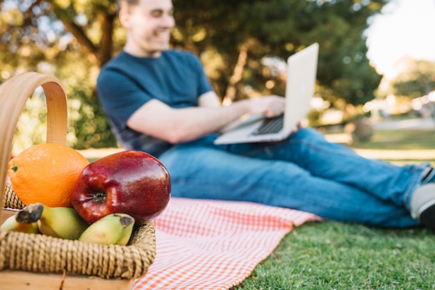 Photo gratuite panier de fruits près de l'homme avec un ordinateur portable