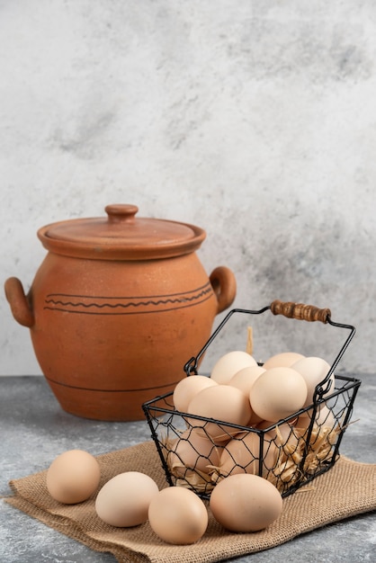 Panier en métal d'oeufs de poule crus et vase antique sur une surface en marbre.