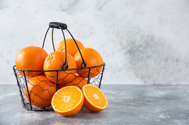 Un panier noir métallique plein de fruits orange juteux sur table en pierre.