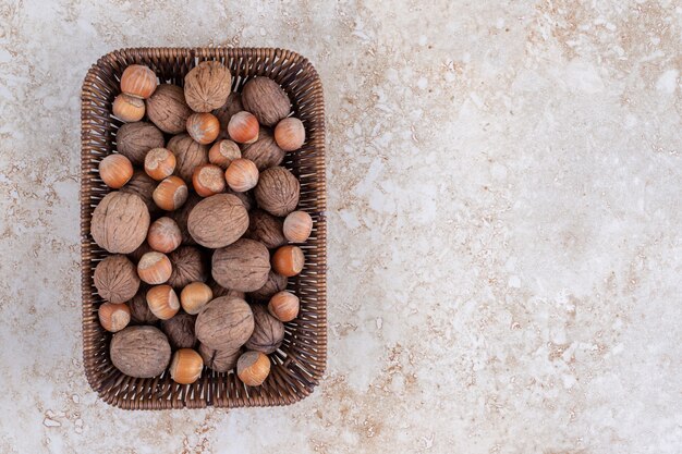 Panier en osier de noix et noisettes décortiquées sur table en marbre.