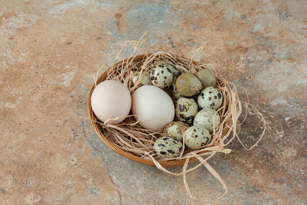 Panier en osier plein avec des œufs de caille sur table en marbre.