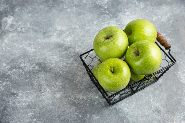 Panier plein de pommes vertes brillantes sur table en marbre.