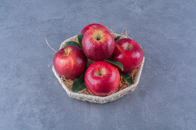 Un panier de pommes et de feuilles sur une table en marbre.