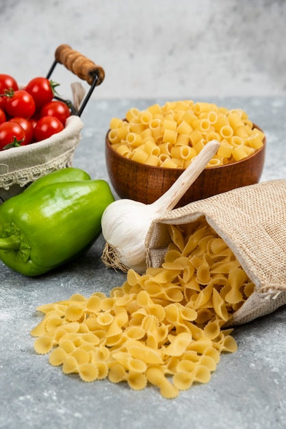 Photo gratuite paniers de pâtes rustiques avec tomates cerises, poivre et ail sur une table en marbre.