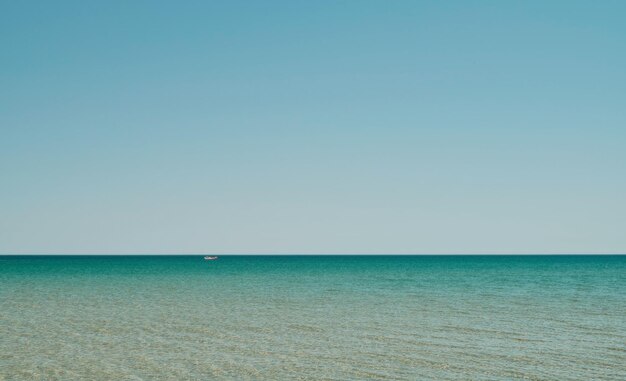 Panorama de la mer dans les eaux peu profondes avec reflet du soleil dans l'eau vaste mer ouverte avec ciel clair ondulation vague et mer calme avec une belle lumière du soleil Le bateau rouge est visible à distance Fond d'écran ou idée de bannière