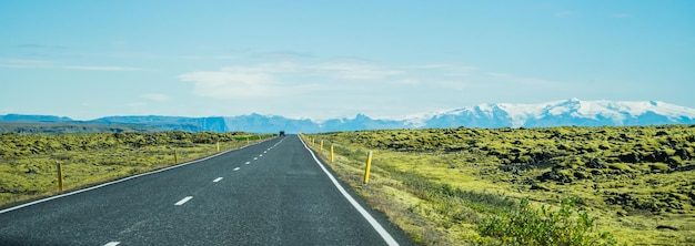 Panoramique d'une longue route goudronnée entourée de champs herbeux en Islande
