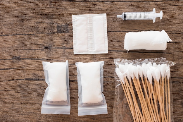 Pansement en gaze de coton médical blanc; seringue et paquet de coton-tige sur une table en bois