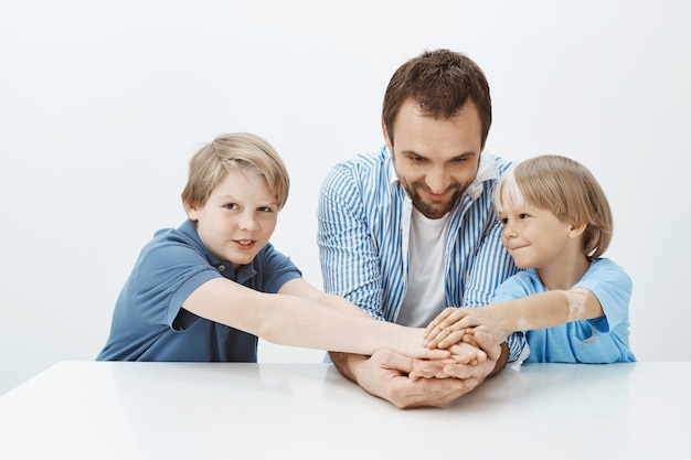 Papa et fils non seulement de la famille mais aussi de l'équipe. Portrait d'heureux frères et sœurs et père se tenant la main alors qu'il était assis à table, souriant largement