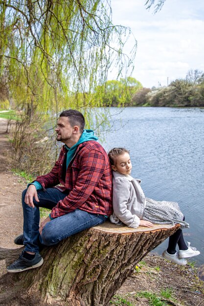 Papa et sa petite fille sont assis dans la forêt au bord de la rivière au début du printemps et profitent de la nature.