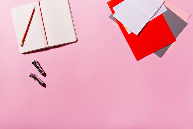 Papeterie colorée et carnet ouvert sont à côté des rouges à lèvres sur le mur rose