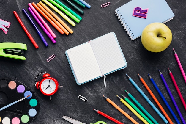 Photo gratuite papeterie lumineuse, horloge et pomme autour de cahier sur fond gris