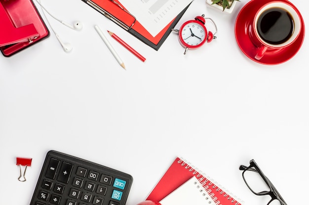 Papeterie rouge, réveil et calculatrice sur un bureau blanc