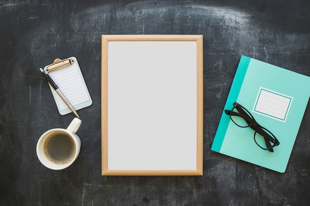 Papeterie; tasse à café; carnet; lunettes et cadre photo blanc sur tableau noir