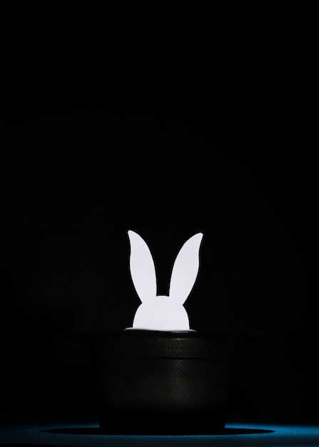 Papier blanc découpé des têtes de lapin dans le haut chapeau noir sur fond noir