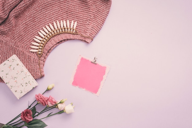 Papier blanc avec des fleurs roses, collier et chandail sur la table