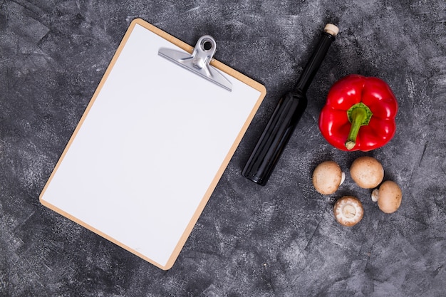 Papier blanc sur le presse-papiers avec du poivron; champignon et bouteille sur fond texturé noir