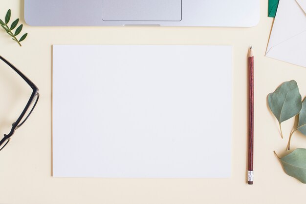Papier blanc vierge; crayon; lunettes; feuilles et ordinateur portable sur fond beige