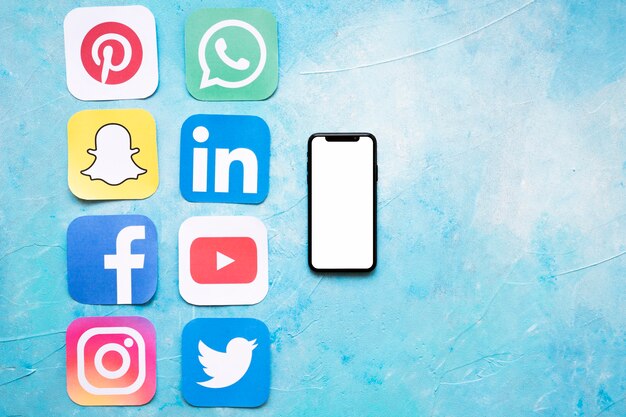 Papier découpé des icônes de médias sociaux disposées près de smartphone