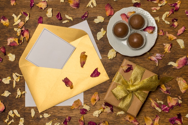 Papier en lettre près de la plaque avec des bonbons et boîte présente entre les feuilles sèches
