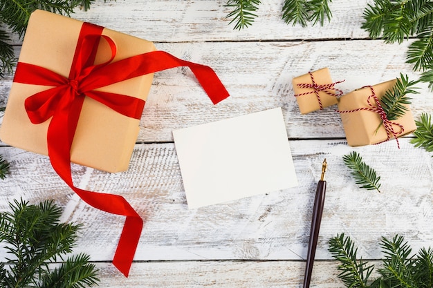 Papier près de brindilles de sapin, stylos et boîtes à cadeaux