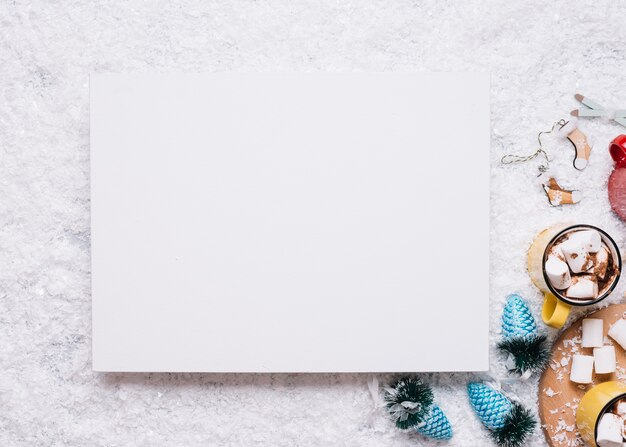 Papier près de tasses avec des guimauves et des jouets de Noël sur la neige