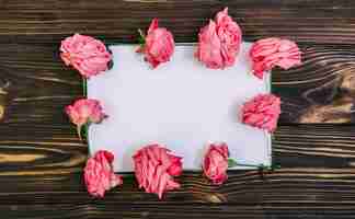 Photo gratuite papier vide avec des roses roses sur une table en bois texturée