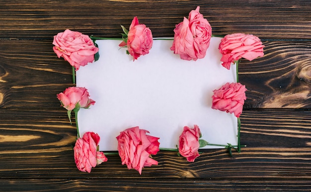 Papier vide avec des roses roses sur une table en bois texturée