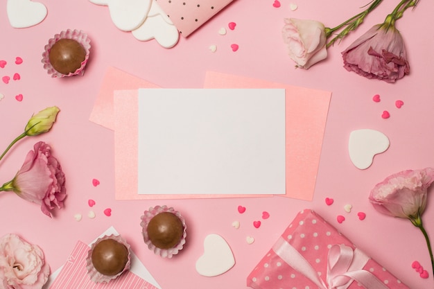 Papiers entre des fleurs près de la boîte présente et des bonbons au chocolat