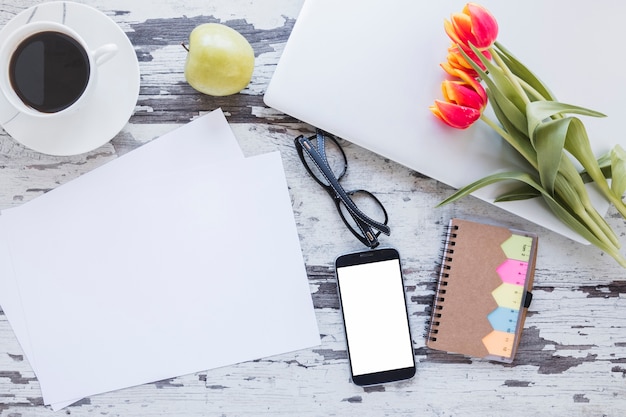 Photo gratuite papiers et tasse à café près de smartphone sur le bureau avec des fleurs de tulipes