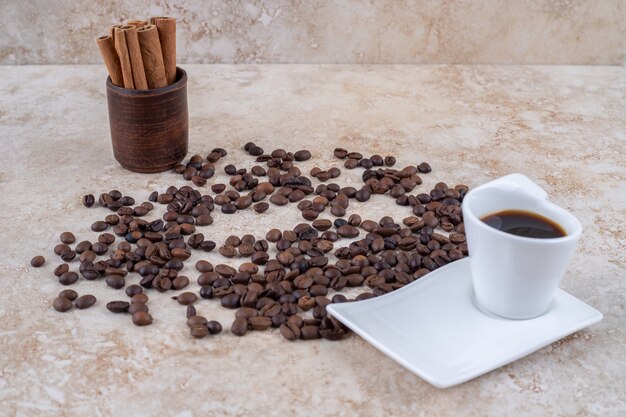 Paquet de bâtons de cannelle dans une tasse en bois à côté de grains de café éparpillés et une tasse de café