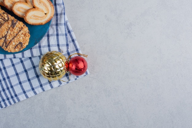 Paquet de cookies sur un tableau bleu à côté de boules de Noël sur une serviette sur la surface en marbre