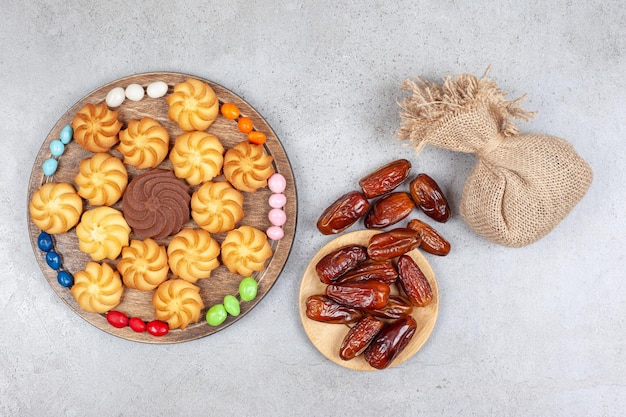 Un paquet de dattes et un sac avec une planche en bois de bonbons et biscuits disposés de façon décorative sur fond de marbre. Photo de haute qualité