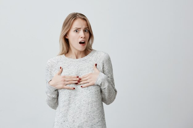 Pardon? Jeune femme offensée perplexe avec des cheveux teints en blonde se montrant avec les mains, se sentant confuse