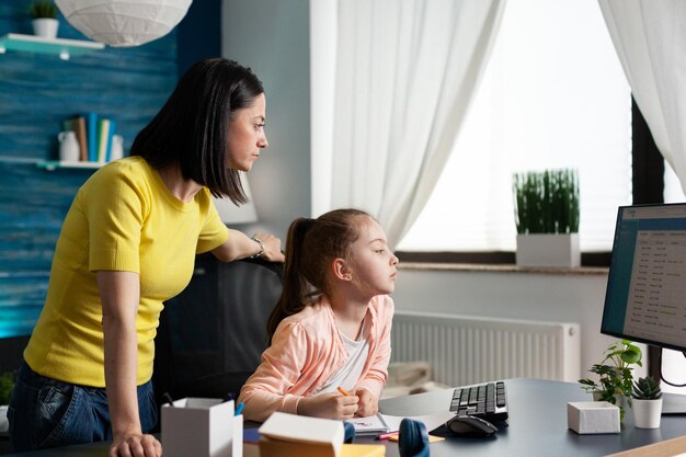 Un parent joyeux aide sa fille à faire ses devoirs scolaires en analysant le cours de mathématiques en ligne ensemble à l'aide d'une plate-forme d'apprentissage en ligne académique dans le salon. Écolier étudiant la littérature. L'enseignement à distance