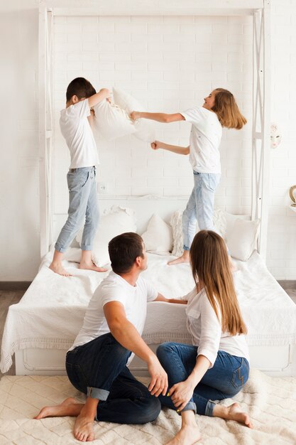 Un parent regarde ses enfants se battre sur un lit à la maison