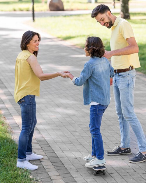 Les parents aident le garçon à utiliser la planche à roulettes dans le parc