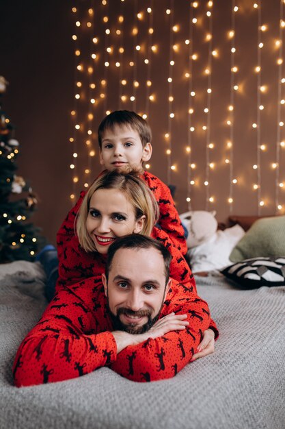 Des parents attrayants et leur petit fils en pull-over rouge s&#39;amusent sur le lit avant un Christ