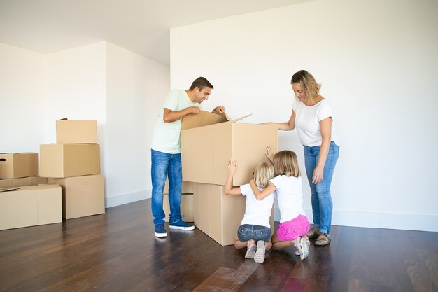 Des parents et deux filles s'amusant en ouvrant des boîtes et en déballant des choses dans leur nouvel appartement vide