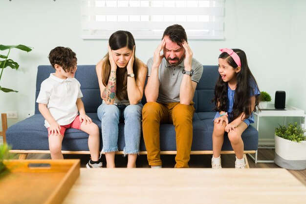 Des parents fatigués et en colère qui se couvrent les oreilles pendant que leurs petits enfants mal conduits agissent. Petits frères et sœurs criant et se sentant en colère