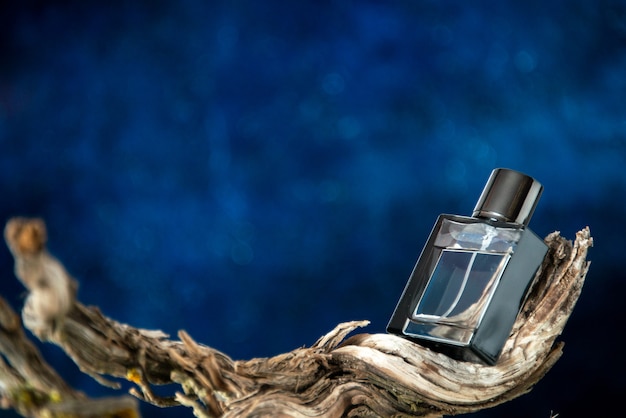 Photo gratuite parfum homme vue de face sur une branche de bois pourri sur fond bleu foncé