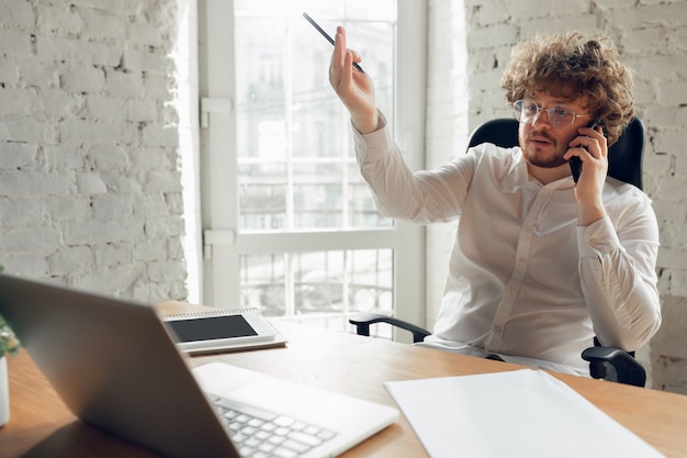 Photo gratuite parler au téléphone. jeune homme caucasien en tenue d'affaires travaillant au bureau