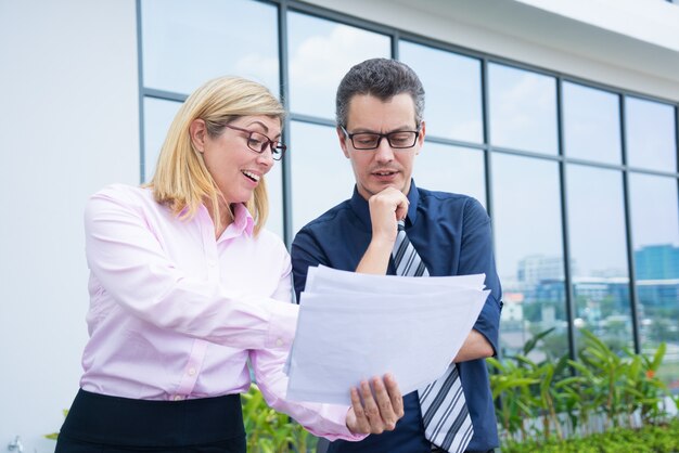 Les partenaires commerciaux du contenu discutent des documents en dehors du bureau.