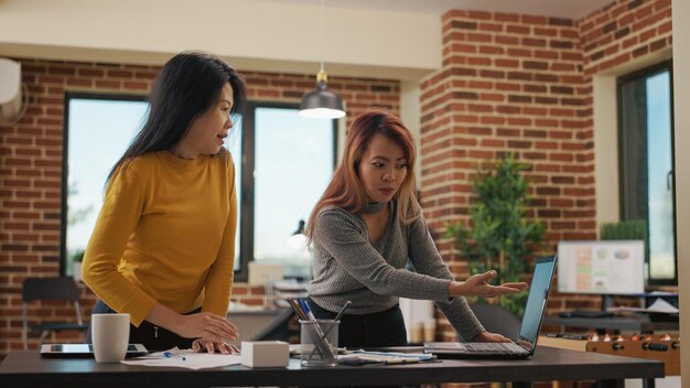 Partenaires commerciaux examinant l'analyse marketing sur ordinateur portable, effectuant des recherches pour planifier une nouvelle application de projet pour la croissance financière. Femmes asiatiques utilisant les statistiques de vente pour travailler sur la gestion