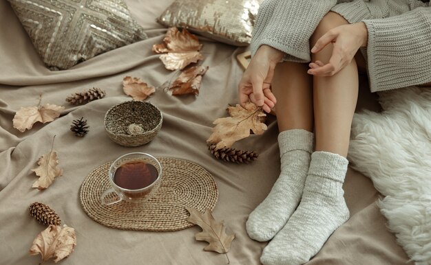 Une partie du corps, une femme dans un lit douillet avec une tasse de thé parmi les feuilles d'automne.