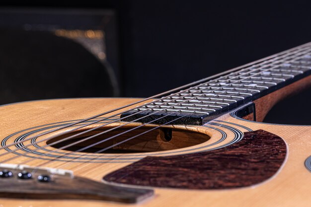 Partie d'une guitare acoustique, manche de guitare avec cordes sur fond noir.