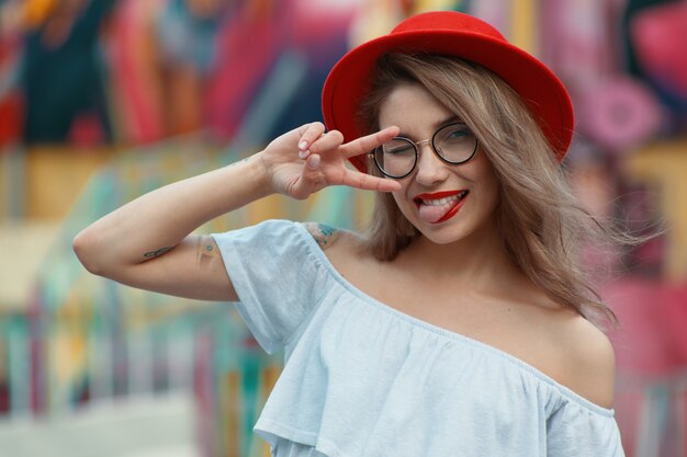 Party girl clins de œil et montrer la langue tout en montrant le signe de la victoire