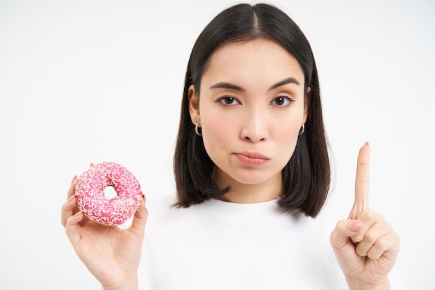 Photo gratuite pas de bonbons jeune femme sérieuse au régime montrant un geste d'arrêt et un beignet glacé désapprouvent la malbouffe