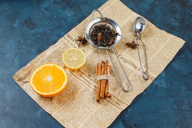 Passoires à thé avec un citron, une orange, un journal et de la cannelle