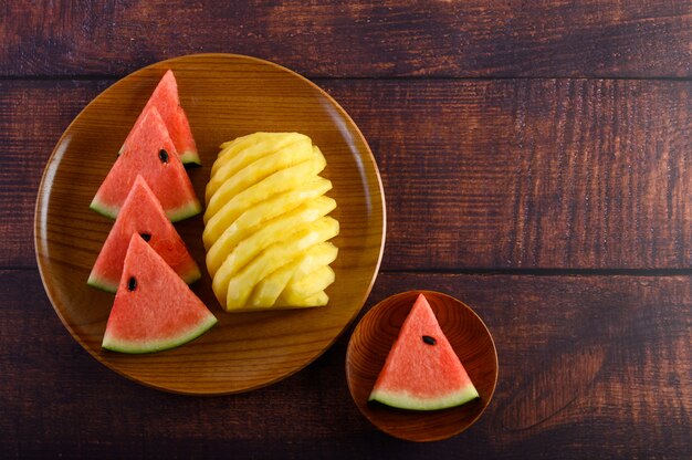 Pastèque et ananas coupés en morceaux sur une plaque de bois